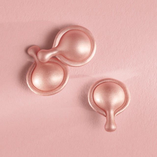 Three Retinol + HPR Ceramide Capsules scattered on a pink background
